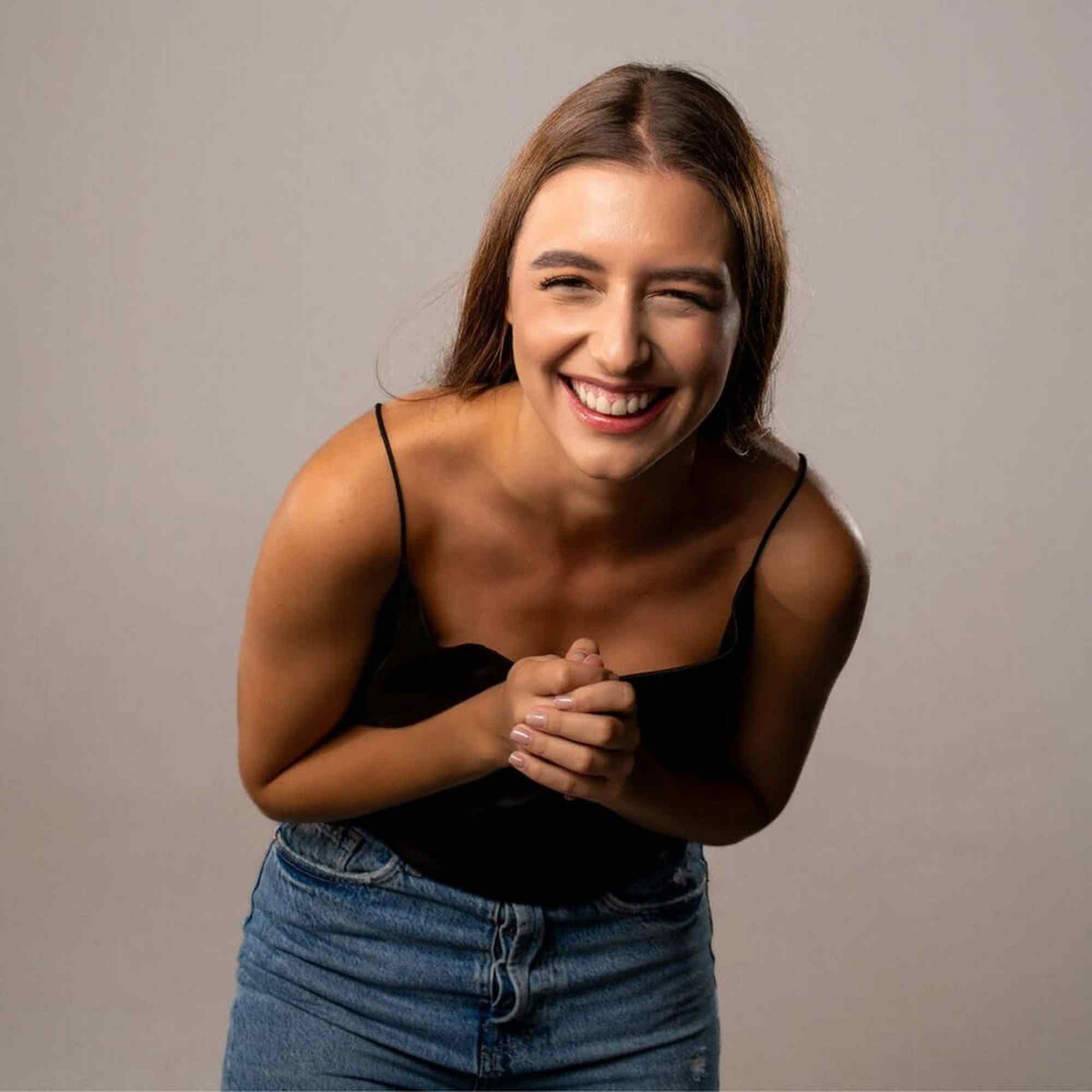 Laughing woman wearing a black top and jeans, exuding joy and warmth, showcasing a cheerful demeanor.