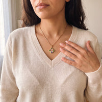 Thumbnail for Woman in a cream V-neck sweater, hand on her chest, wearing the gold secret clover photo necklace | SKU: TPH-CLVN-GOLD